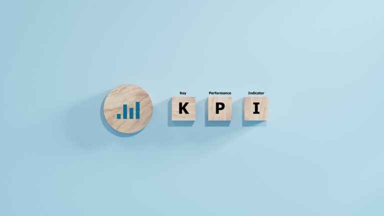 Wooden blocks on a blue background spell out KPI, with smaller text Key Performance Indicator above each letter. A wooden circle with a bar graph icon, symbolizing Operational KPIs, appears on the left.